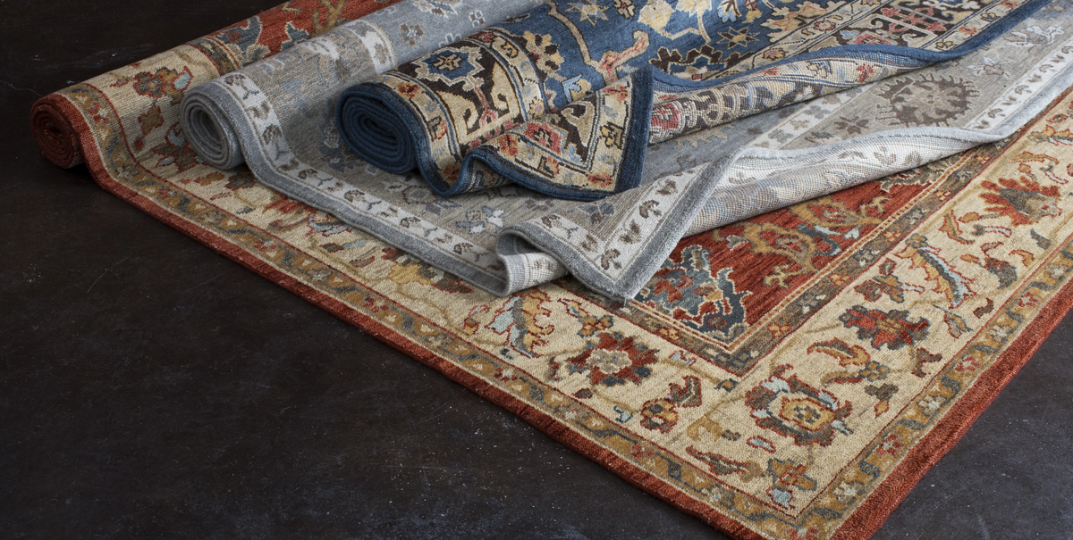 Two ornate patterned area rugs displayed on a dark floor, with one partially rolled up to show the underside and the other laid flat to display the full design.