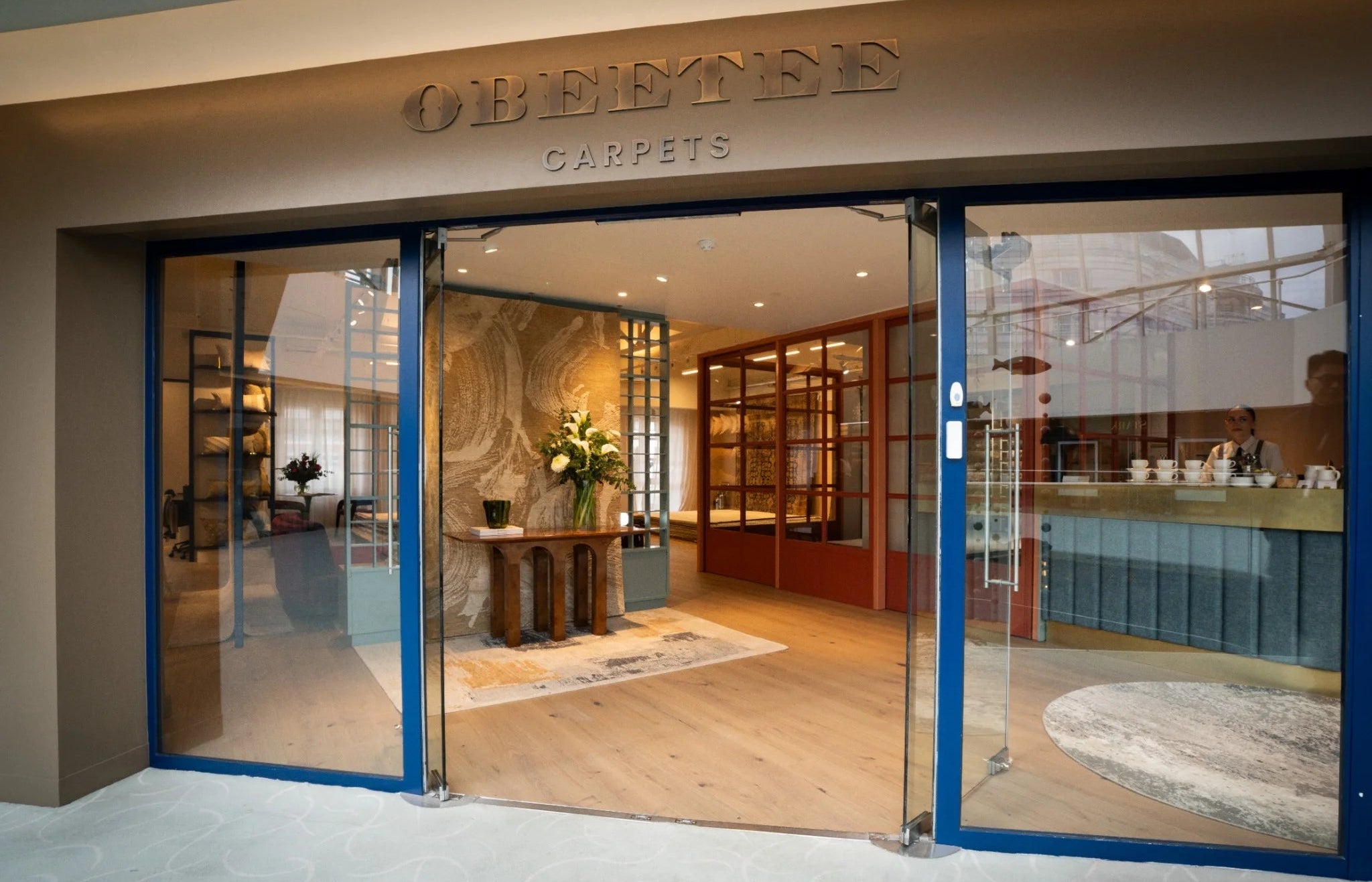 Storefront with glass doors displaying interior decor, including carpets and furniture.